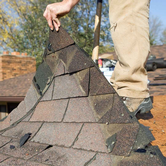 Roofer lifting damaged asphalt shingles by hand during a storm damage roof inspection in Hickory, North Carolina