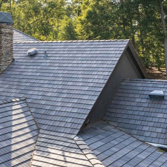 Gray slate-style roof with a stone chimney and roof vents, surrounded by tall trees