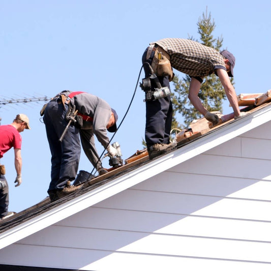 Roofing crew installing a new roof on a steep pitch above white siding