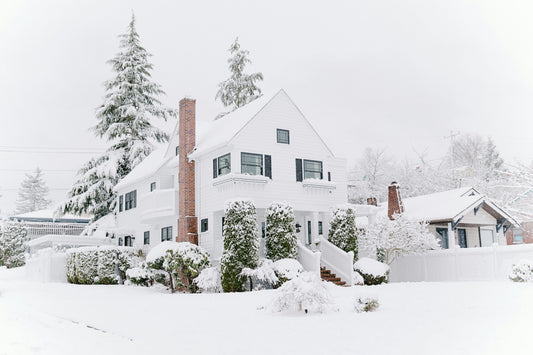 White two-story house with a brick chimney and a snow-covered roof after a winter storm